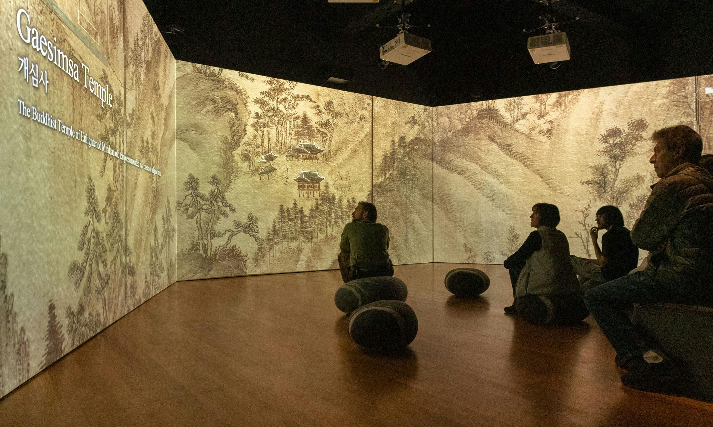 people sitting in a room amidst a large immersive projection 